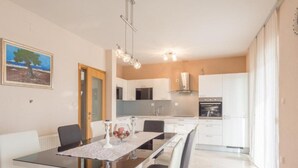 A modern kitchen with white cabinets, a stainless steel range hood, and a dining area with a glass table and chairs. - Holiday House Balen With Swimming Pool (Benkovac)