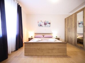 A bedroom with a wooden bed, a nightstand, a wall-mounted painting, and a wardrobe. - Villa Maja (Škabrnja)