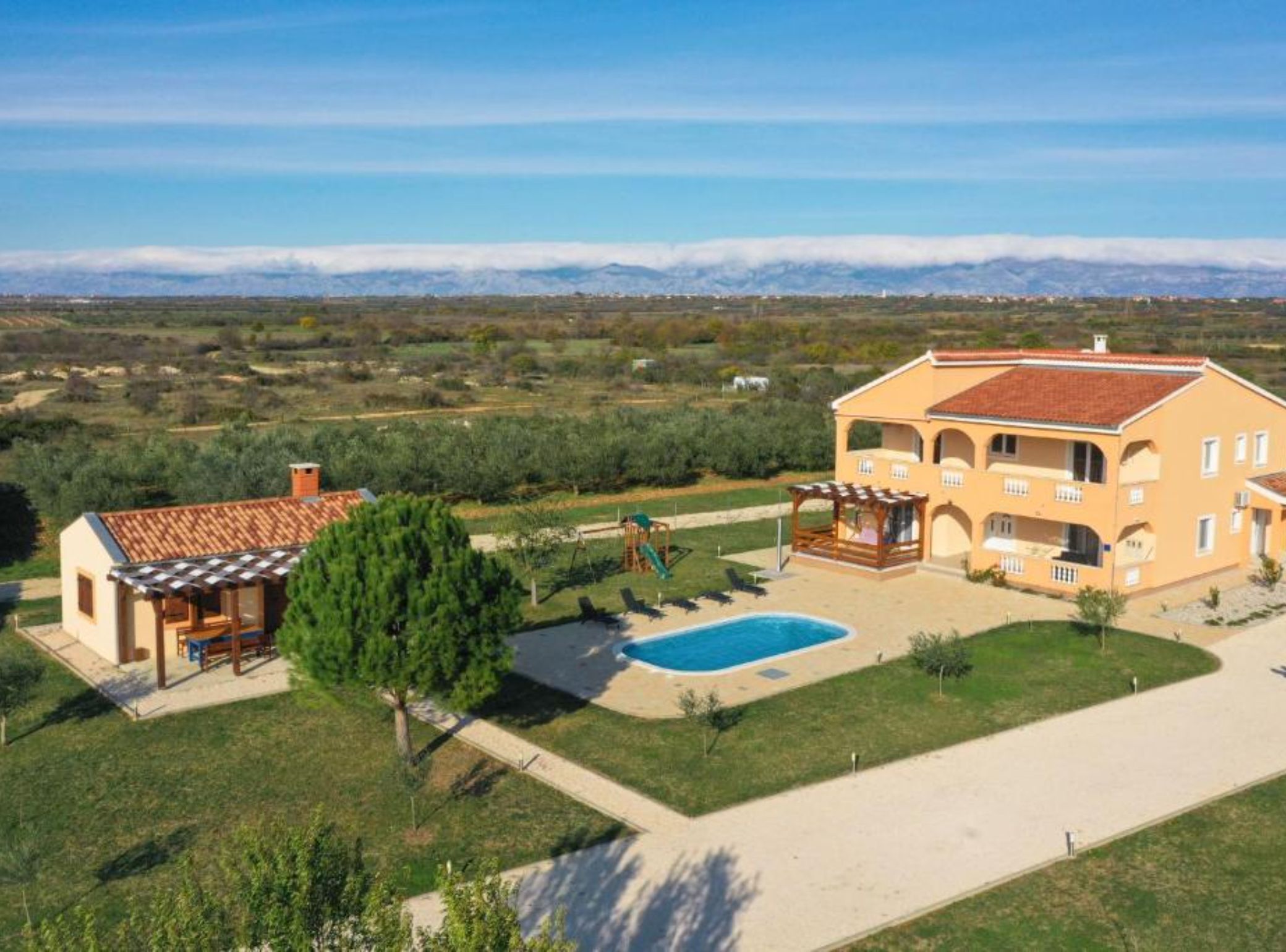 A two-story house with a swimming pool, a patio, and a view of mountains in the background.