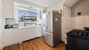 A kitchen with white cabinets, a stainless steel refrigerator, a stove, and a window with blinds. - Fantastic 5-bedroom house with AC in charming Highland Park (Highland Park)