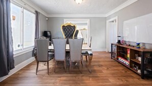 A dining area with a table and chairs, a decorative chair, a shelf with items, and a view through a window. - Fantastic 5-bedroom house with AC in charming Highland Park (Highland Park)