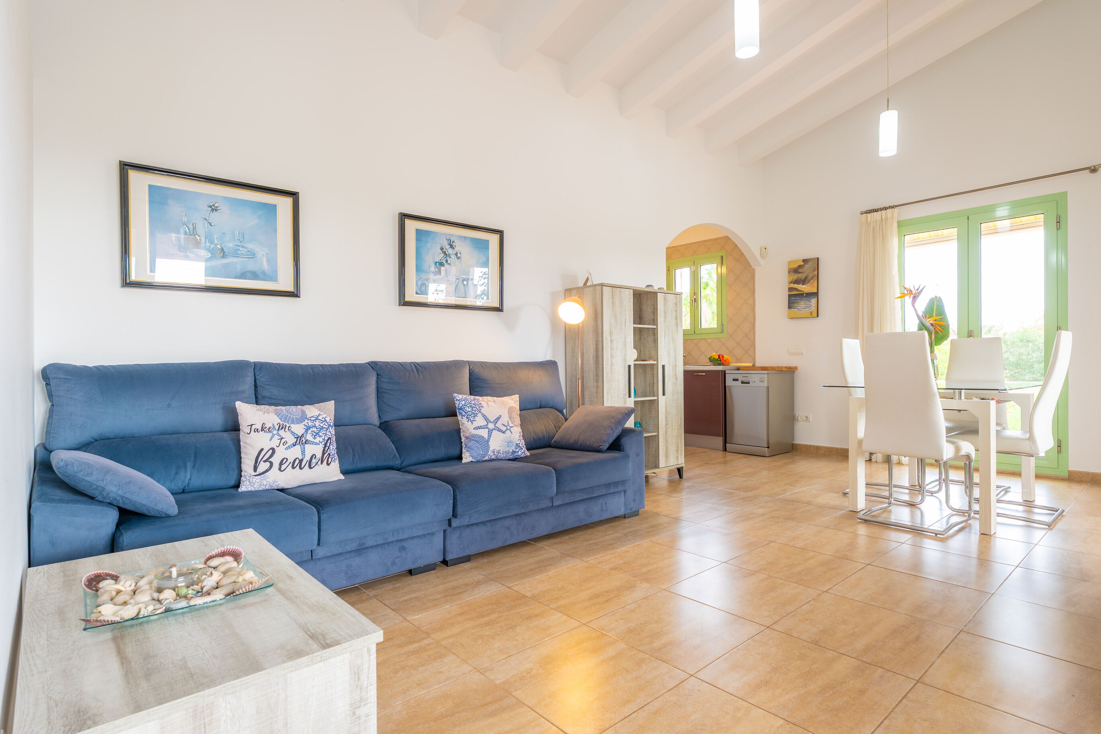 Ein Wohnzimmer mit einem blauen Sofa, einem Glastisch und einem Essbereich mit weißem Tisch und Stühlen.