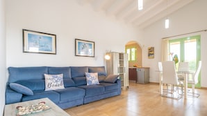 A living room with a blue sofa, a glass coffee table, and a dining area with a white table and chairs. - SA PLANA DE BAIX - Cozy house in Son Servera with free wifi. (Son Servera)
