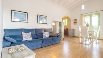 Ein Wohnzimmer mit einem blauen Sofa, einem Glastisch und einem Essbereich mit weißem Tisch und Stühlen.