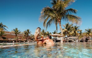 A couple in a clear pool with palm trees and resort buildings in the background. - Elite Oceanfront Penthouse - 2 Bed 3 Bath: Danzante Bay: TPC Golf Course (Loreto)