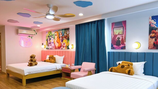 A room with two beds, a ceiling fan, a neon bear sign, and colorful wall art. - Casa de Capybara (Siem Reap)