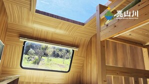 L’intérieur d’un chalet en bois, avec un lit, une fenêtre donnant sur les arbres et le logo du parc de loisirs Linds & Stream Resort.