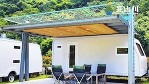 Un espace extérieur aménagé avec une table et des chaises, protégé par un auvent, et situé à côté d’un camping-car blanc.