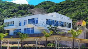 Un bâtiment moderne à deux étages, doté de grandes fenêtres et d’un toit plat, entouré d’une végétation luxuriante et agrémenté d’une structure sphérique décorative.