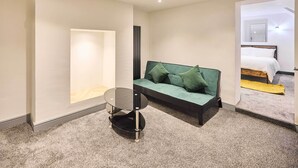 Ein modernes Hotelzimmer mit einem grünen Sofa, einem kleinen runden Tisch und einem Bett mit einem Holzkopfende.