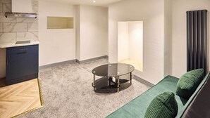 Ein stilvoller Wohnraum mit Küche, einem runden Glastisch, einem grünen Sofa mit Kissen und Blick ins Freie.