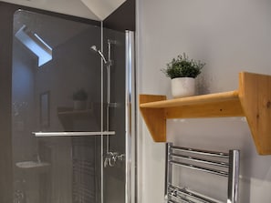 Un baño con cabina de ducha de vidrio, un estante de madera con una planta en maceta y un perchero de cromo.
