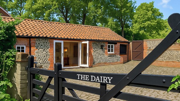 Un edificio de ladrillo con techo de tejas, puerta de cristal y un portón con la leyenda 'THE DAIRY'.
