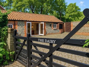 A brick building with a tiled roof, a glass door, and a gate labeled 'THE DAIRY.' - 1 bedroom accommodation in North Walsham (North Walsham)