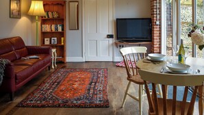 Una sala de estar con un sofá de cuero, una estantería, un televisor y un comedor con una mesa y sillas.