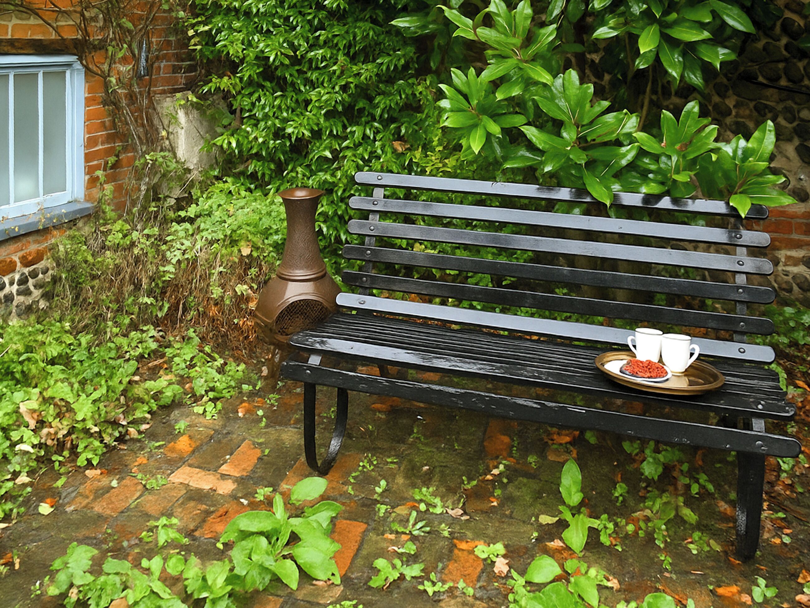 A black bench with a tray of food and two white cups.