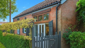 A brick house with a grey fence, a window with a white frame, and a door with a glass panel. - The Coach House - UK50884 (North Walsham)