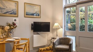 A living room with a television, a radiator, a lamp, a chair, and a dining table set with plates and a vase of flowers. - The Coach House - UK50884 (North Walsham)