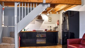 A kitchen with a stove, oven, and refrigerator, a red leather sofa, and a staircase leading to a loft area. - The Coach House - UK50884 (North Walsham)