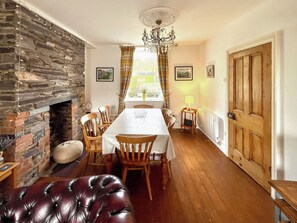 A dining room with a stone fireplace, wooden chairs, a table, and a chandelier. - A traditional Welsh cottage beside Nantlle Lake in the stunning Nantlle Valley. (Nantlle, near Caernarfon)