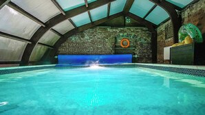 An indoor swimming pool with a clear blue water surface, a brick wall with a lifebuoy, and a blue safety mat. - 6 bedroom accommodation in Market Rasen (Market Rasen)