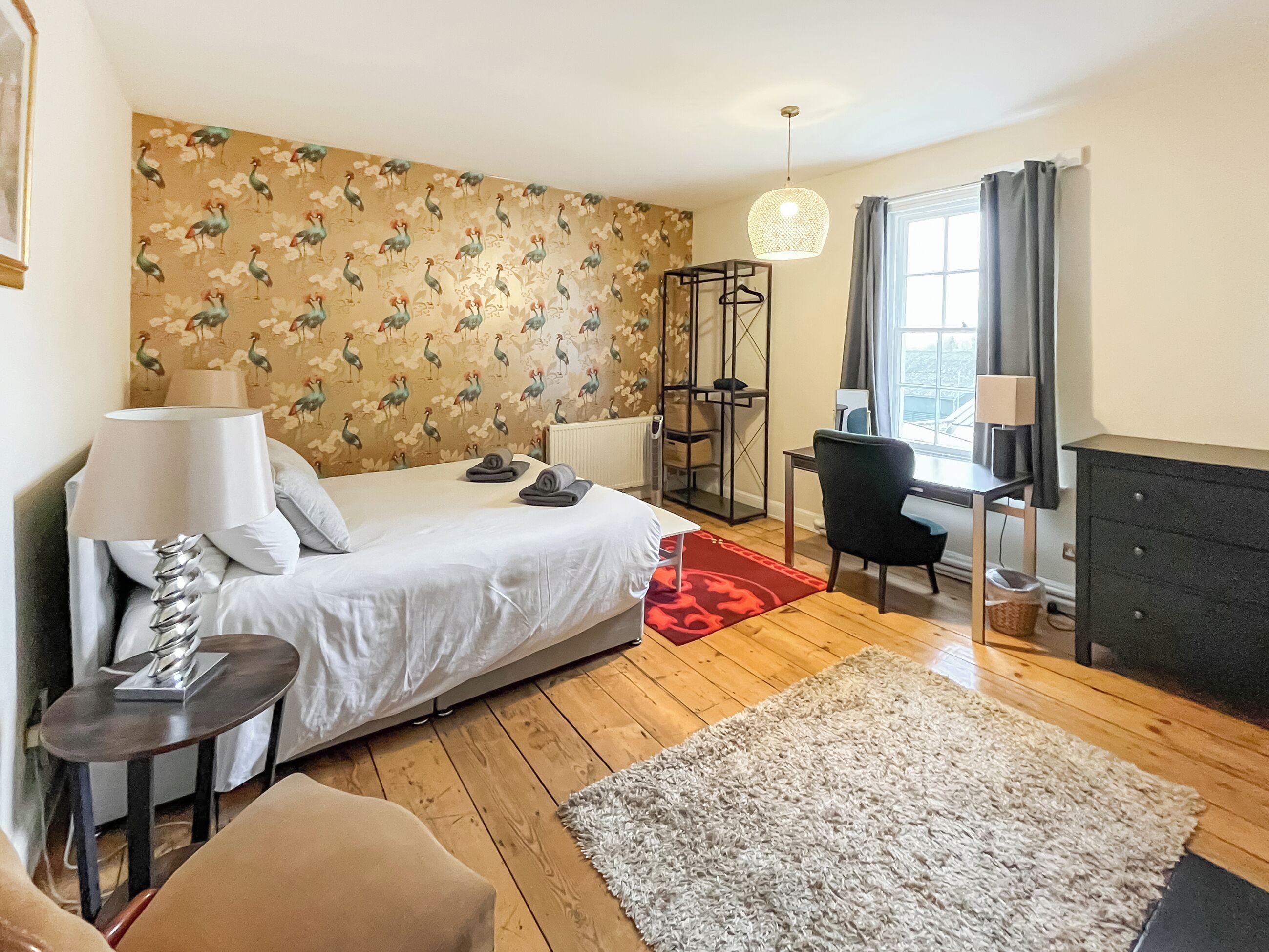 A bedroom with a bed, bedside table, lamp, desk, chair, and a dresser.