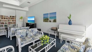 Ein modernes Wohnzimmer mit weißen Möbeln, einem Bücherregal, einem Flachbildfernseher und einem Klavier.