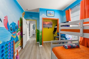 Habitación infantil con una litera, un mural en la pared y una puerta que da a otra habitación.