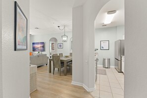 Une cuisine moderne équipée d’un réfrigérateur, un coin repas avec une table et des chaises, et un salon avec un canapé et un téléviseur.