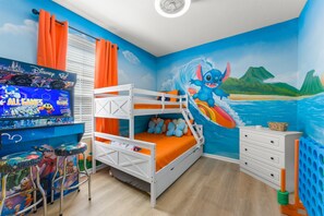 Una habitación infantil con literas, un mural con temática de Disney, un televisor y una zona de juegos.