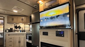 Cocina compacta para camper con televisor de pantalla plana sobre la chimenea empotrada, armarios de madera y microondas.