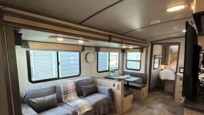 Interior compacto de autocaravana con kitchenette, zona de comedor y área de descanso con sofá y mesa.