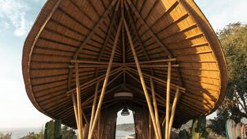 A large, open pavilion with a triangular roof structure, surrounded by a stone pathway and palm trees.