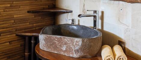 Un baño rústico con lavamanos de piedra, listones de madera y un espejo con marco de madera.