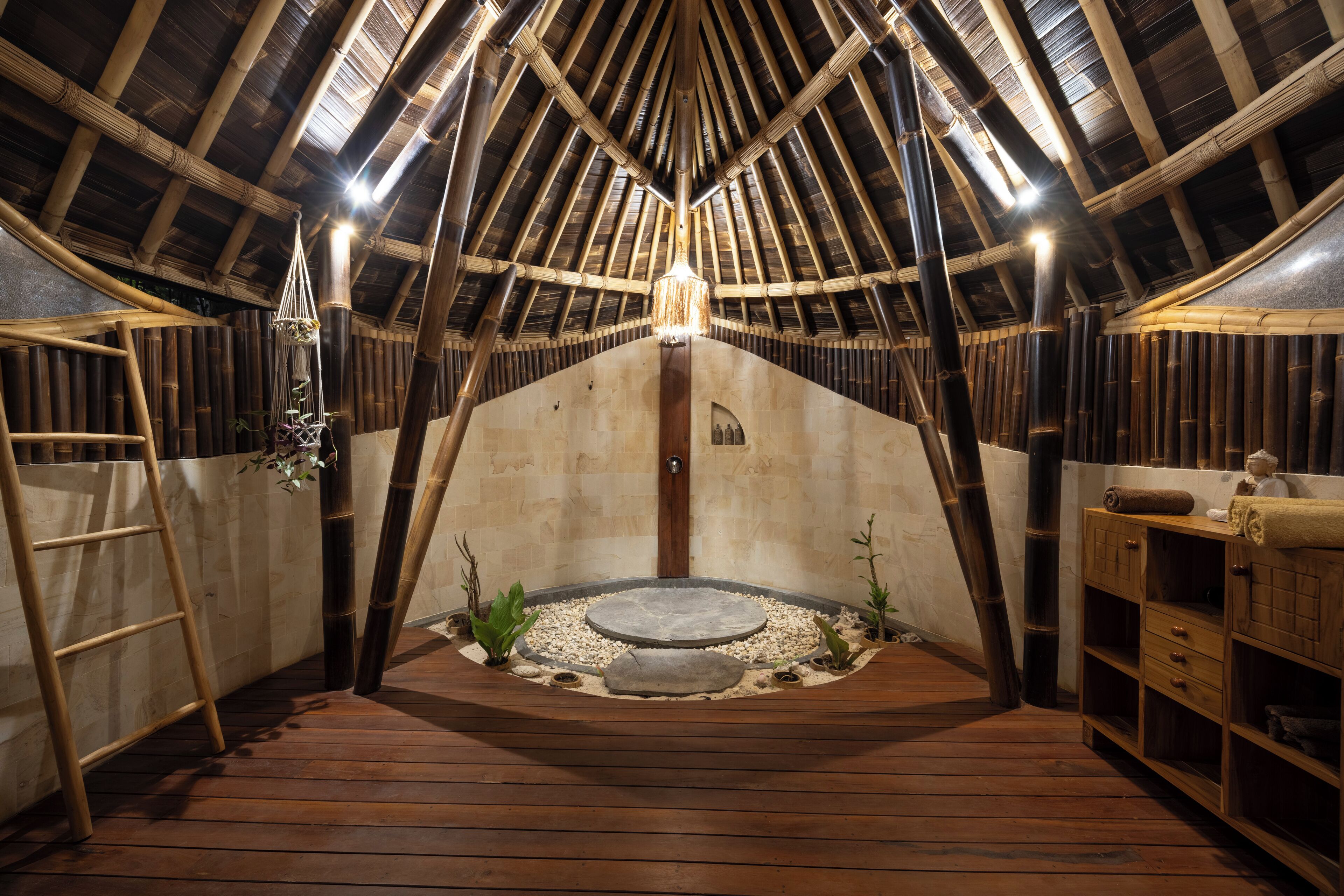 An attic room with a sloped ceiling, wooden beams, a central light fixture, a small circular stone feature, and a wooden ladder.