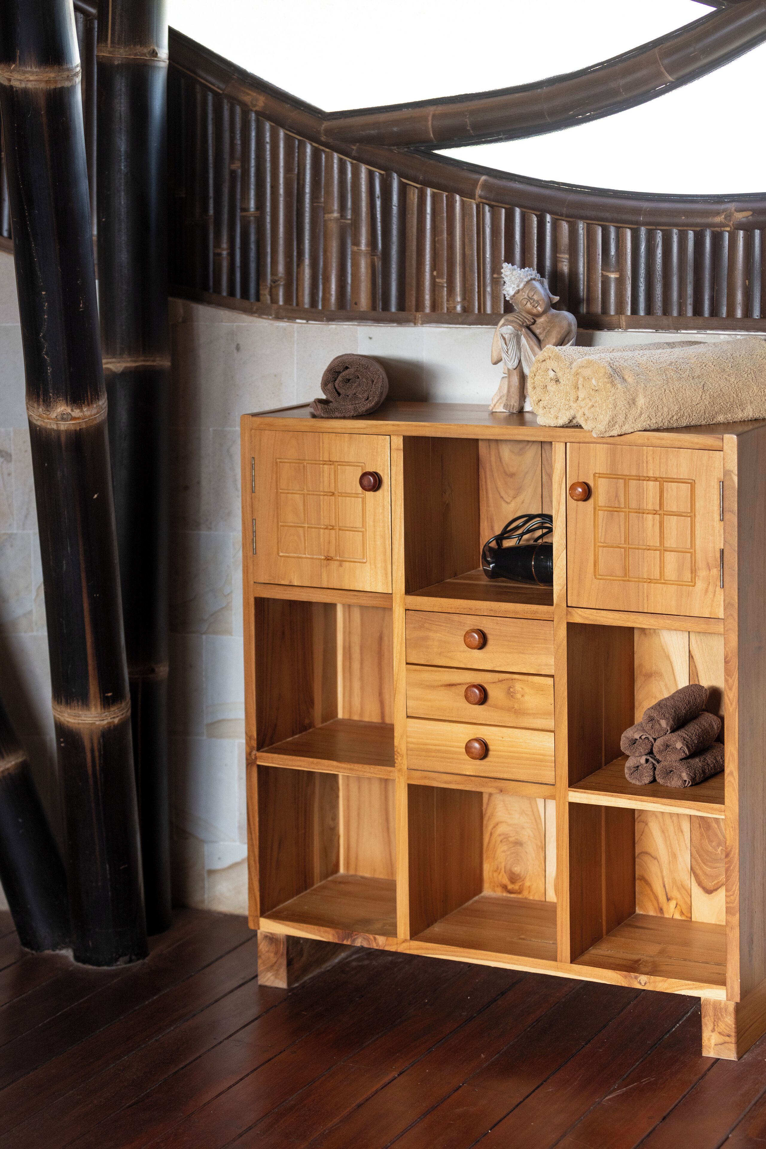 Een houten kast met meerdere lades en planken, geplaatst tegen een bamboe wand.