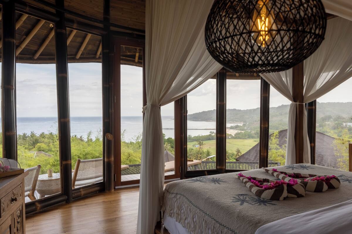 A bedroom with a large bed, a view of the sea, and a hanging light fixture.