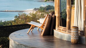 Una terraza de madera con vistas al mar y colinas, una silla de descanso y un jarrón decorativo.