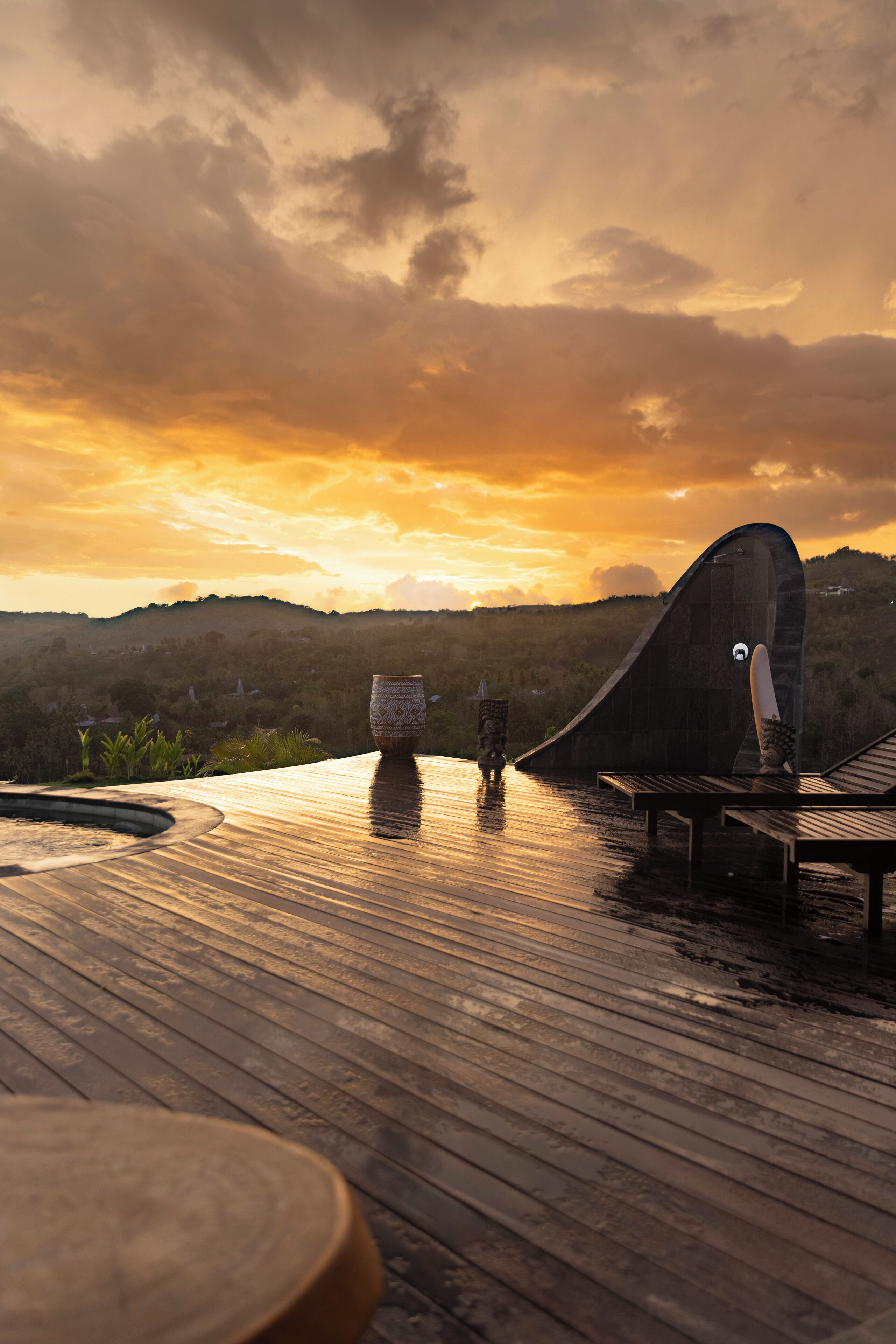 Una terraza de madera con una estructura curva, un jarrón grande y un banco.