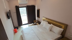 Camera d'albergo con un ampio letto, una televisione a parete, un tavolino e una finestra con tende.