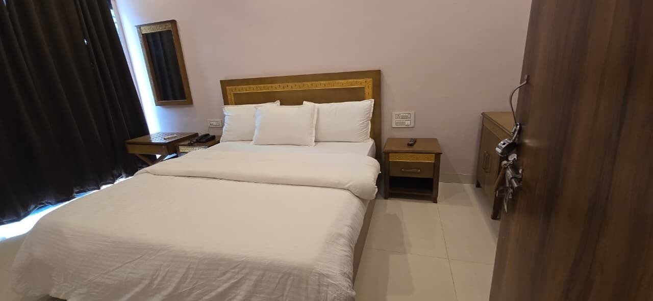 A hotel room with a large bed, two bedside tables, a nightstand, a mirror, and a door with a handle.
