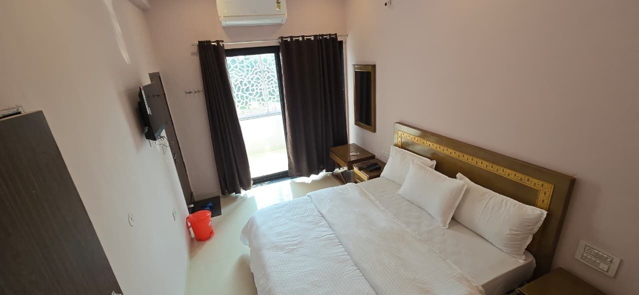 Habitación de hotel con una cama grande, un televisor en la pared, una mesita y una ventana con cortinas.