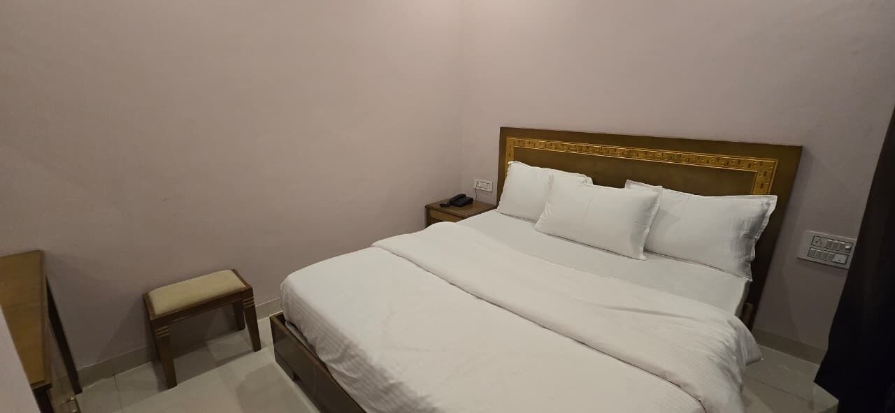 A neatly made bed with white linens and pillows, a bedside table with a lamp, and a small wooden bench.