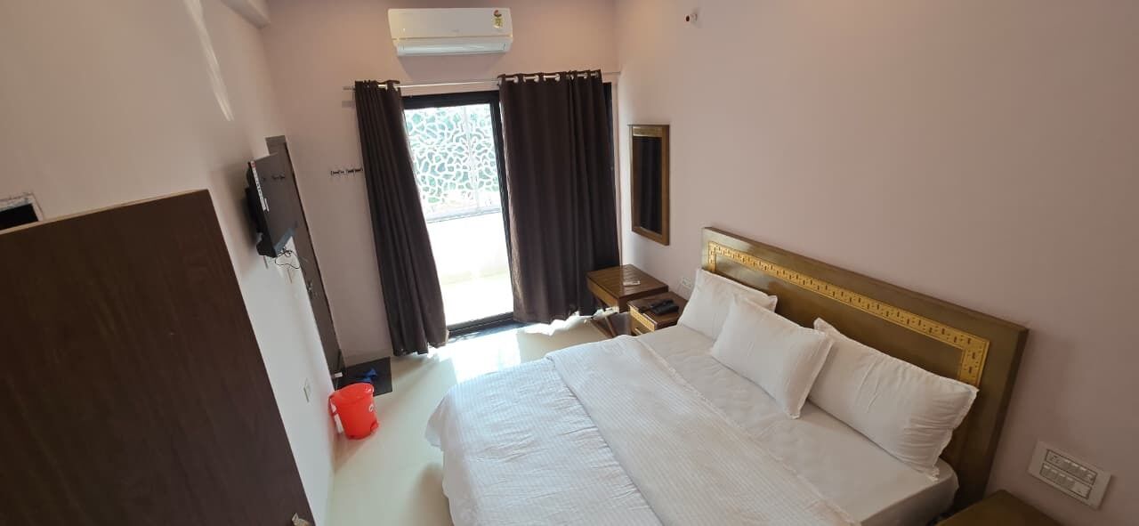 A hotel room with a large bed, a bedside table, a TV, and a window with curtains.