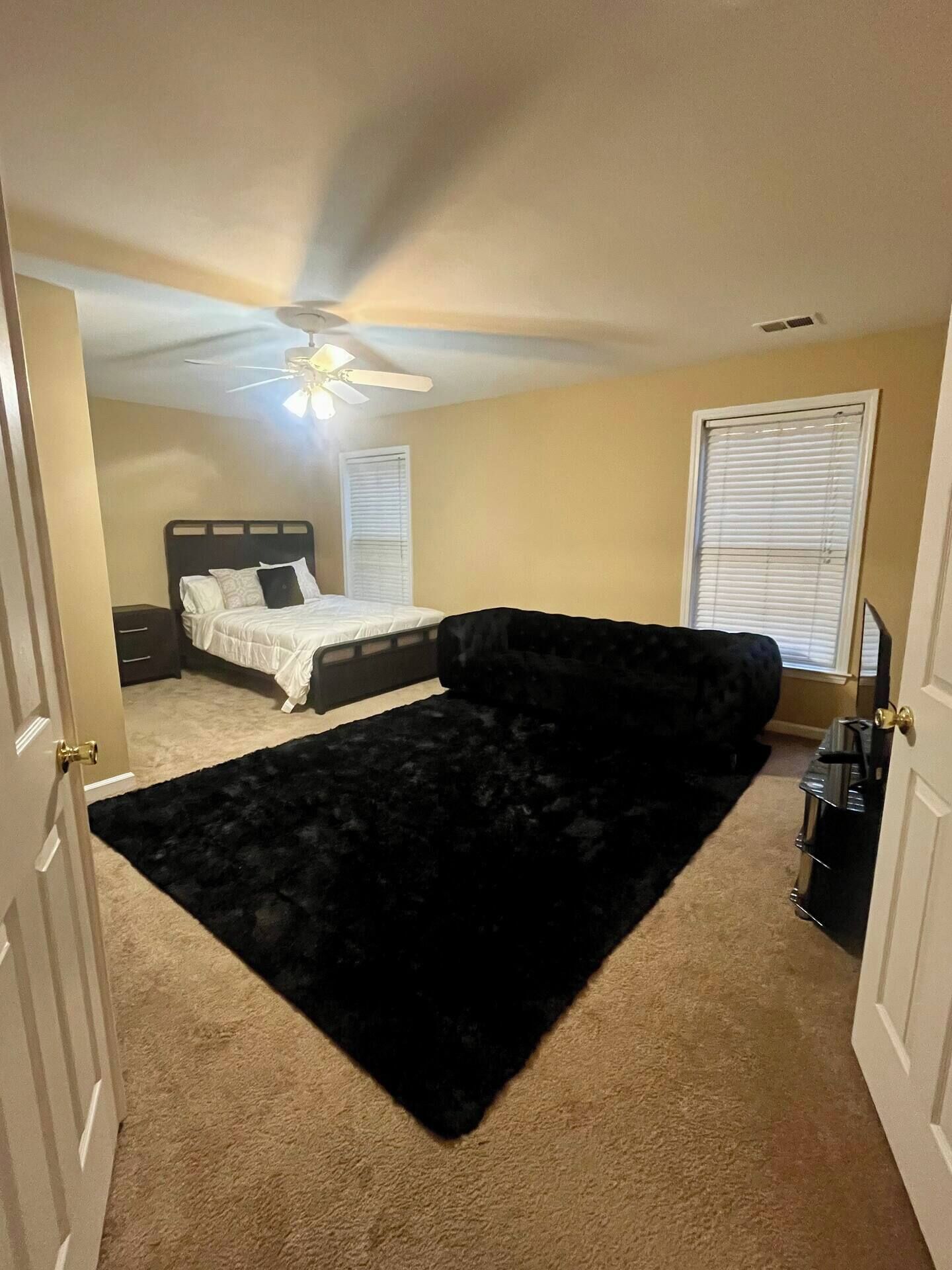 Une chambre à coucher avec un lit, un canapé en velours noir, un ventilateur de plafond et une fenêtre avec des stores.