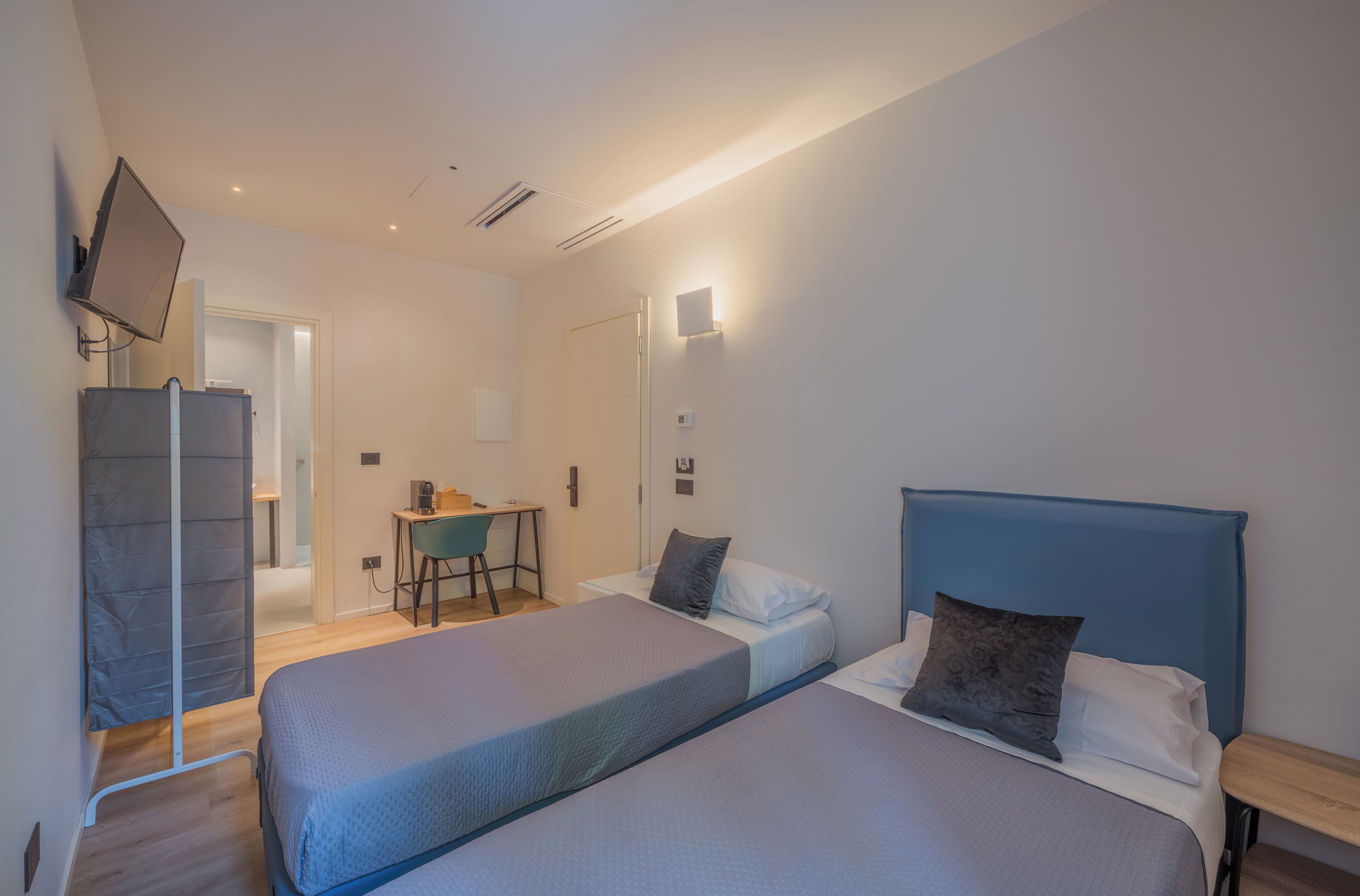 Une chambre avec deux lits, un bureau, une chaise et un téléviseur fixé au mur.