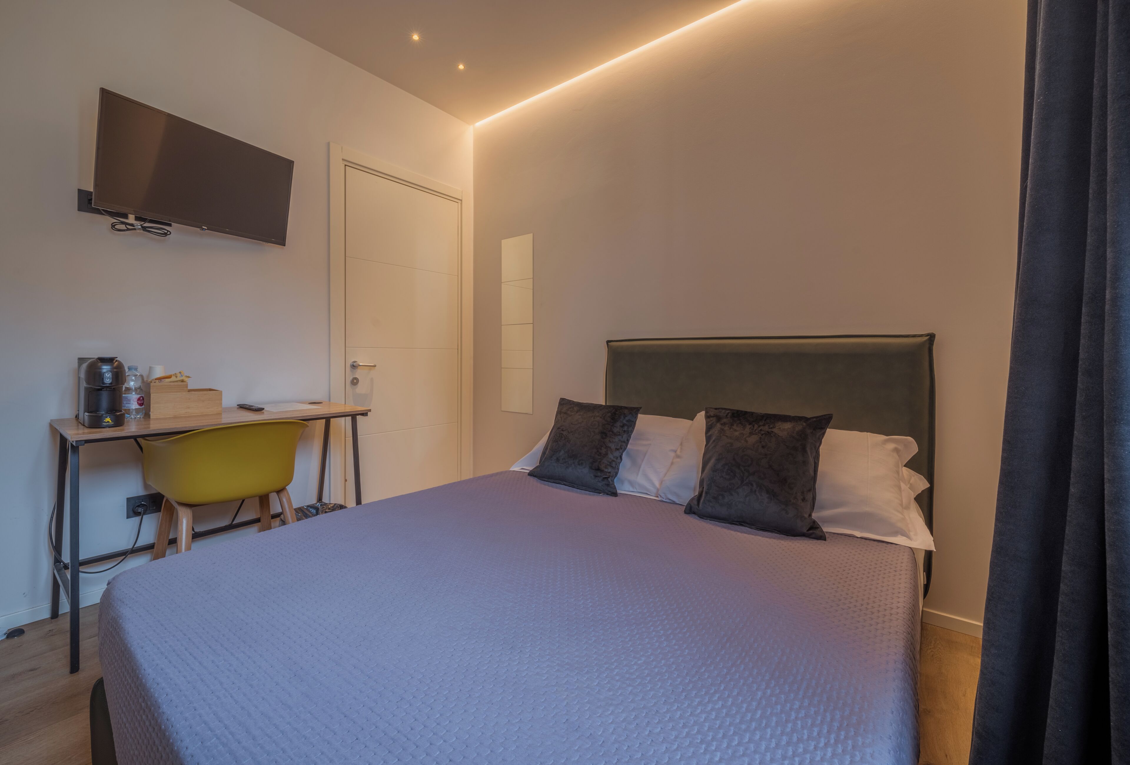 Une chambre à coucher avec un lit, un bureau, une chaise, une télévision et une porte.