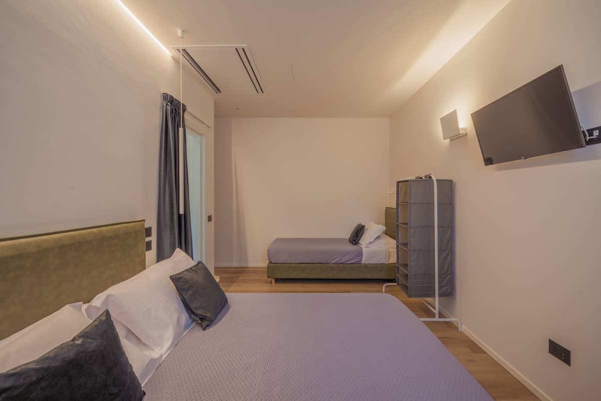 A hotel room with a bed, a smaller bed, a wardrobe, a flat-screen TV, and a ceiling light.