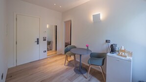 A modern room with a round table, two chairs, a small refrigerator, and a wall-mounted light fixture. - DIMORA IN PRATO (Padova)