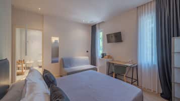Habitación de hotel con cama, escritorio, silla, televisor y baño visible a través de una puerta abierta.